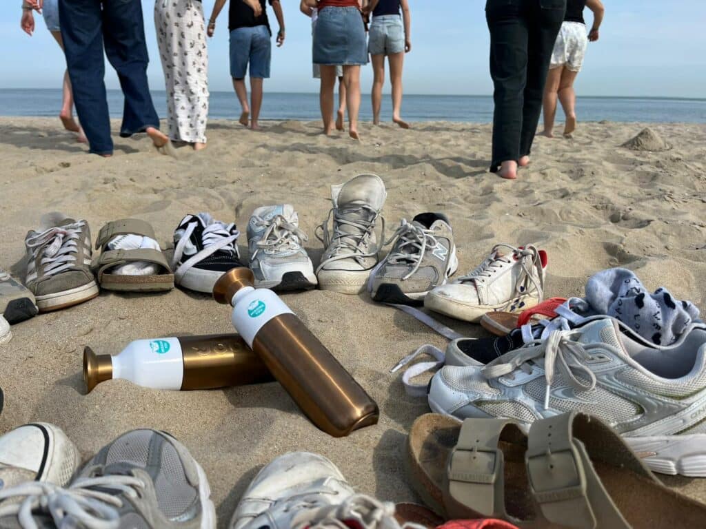 Rij schoenen achtergelaten in het zand terwijl jongeren blootsvoets naar de zee lopen